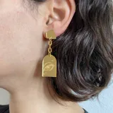 Par de aros colgantes con base negra, cadena plateada y dije transparente con dibujo de ojo rosa.