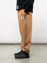 Pantalón de felpa color crema, con corte relajado, costuras verticales en la parte delantera y etiqueta con el logo de Umbro.