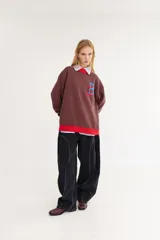 Sweater de punto color amarillo con silueta oversize y estilo universitario vintage. Presenta cuello redondo, puños y ruedo en tejido acanalado de color gris azulado, y un diseño gráfico bordado en el frente.