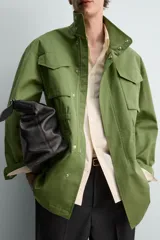 Parka estilo militar color verde, de corte relaxed fit, cuello subido y manga larga. Cuenta con bolsillos de plastrón con solapa en el pecho y en la cadera, cintura ajustable con cordón interior y cierre frontal con cremallera oculta por solapa con botones a presión.