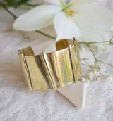 Brazalete ancho de bronce color dorado con diseño de líneas verticales y diagonales en relieve.