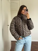 Campera puffer con estampado de leopardo en tonos blanco y negro, cuello alto, cierre frontal y bolsillos laterales.