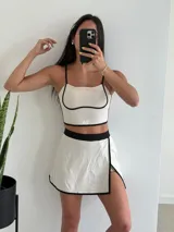 Conjunto deportivo color beige con ribetes negros, compuesto por un top con tirantes finos y una minifalda con short interno.