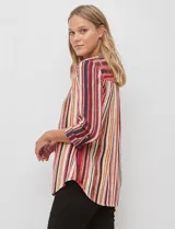 Blusa de gasa con estampado de rayas verticales en tonos rojos, naranjas y cremas. Presenta cuello mao con escote en V, abertura frontal con botones y mangas largas con presilla para regular el largo.
