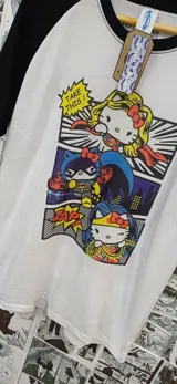 Remera blanca de mangas negras ranglán con estampado de Hello Kitty disfrazada de Superman, Batman y Wonder Woman.