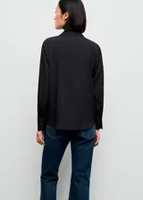 Camisa básica de tejido fluido y color negro, con diseño recto, cuello camisero, manga larga con puños abotonados y cierre delantero con botones.