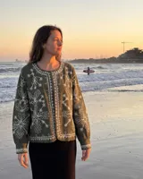 Chaqueta verde oliva de algodón con bordados botánicos en hilo blanco, cuello redondo y cierre frontal de botones.