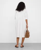 Vestido camisero midi blanco de algodón orgánico, con cuello tipo tira, mangas raglán sobre el codo, botonadura frontal oculta y canesú con pliegues en la espalda.