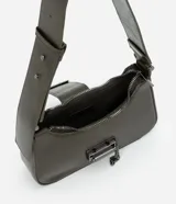 Cartera tipo baguette de la marca Satinato, confeccionada en poliuretano con acabado brillante. Presenta un diseño estructurado con correa ancha, cierre superior con cremallera y un detalle metálico frontal con cadena decorativa.