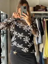 Blusa de microtul negro transparente, con mangas largas y bordados blancos con diseño floral.