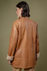 Campera de cuero color tostado con diseño de paneles, cuello alto y puños con forro de corderito sintético. Presenta cierre frontal con botones grandes y bolsillos laterales.