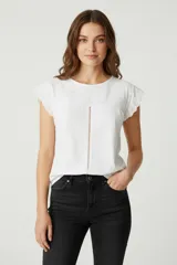 Remera blanca de algodón con cuello redondo, mangas cortas con detalle de encaje y bordado en la parte superior delantera. Presenta una costura vertical central con detalle calado.