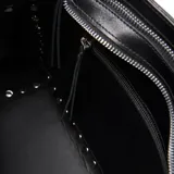 Cartera estructurada de cuero vacuno en color negro, de formato mediano con detalle de tachas metálicas en todo el contorno. Cuenta con asas cortas fijas para llevar en mano y una correa larga regulable y desmontable. Presenta cierre superior con cremallera metálica, costuras decorativas en los paneles frontales, herrajes plateados y bolsillo interior con cierre.