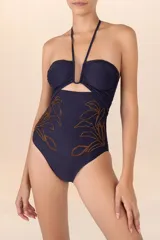 Traje de baño entero azul marino con escote bandeau, tirantes finos que se atan al cuello y bordado floral dorado en la parte inferior.