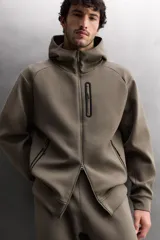 Sudadera con capucha de entrenamiento, confeccionada en tejido técnico de algodón con efecto neopreno. Presenta cierre frontal de cremallera, cuello subido, bolsillos laterales y un bolsillo en el pecho, todos con cierre de cremallera y acabado termofijado.
