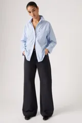 Jean de corte loose boot, tiro medio, color negro, con diseño de cinco bolsillos y cierre frontal con botón y cremallera.