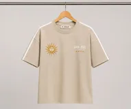 Remera de algodón color beige con diseño de sol bordado y texto en el frente. Presenta dos franjas blancas laterales en las mangas y un corte holgado.