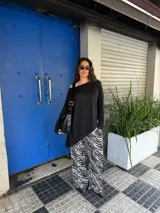 Conjunto de buzo asimétrico de manga larga con hombro descubierto y pantalón tiro alto de pierna ancha con estampado animal print tipo cebra, confeccionados en viscosa.
