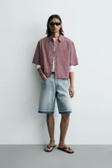 Bermuda de denim de algodón con efecto lavado desgastado en tonos marrones y azules. Tiene tiro medio, diseño de cinco bolsillos, pierna recta de corte holgado y bajo con acabado irregular. Cuenta con cierre frontal de cremallera y botón metálico.