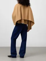 Chaqueta corta color camel con cuello solapa, manga larga japonesa y cierre frontal con botones. Presenta un diseño con capa superpuesta en la espalda.