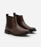 Bota tipo Chelsea de caña media, confeccionada en cuero sintético color marrón oscuro. Presenta punta redonda, paneles laterales elásticos para facilitar el calce y suela de goma robusta.