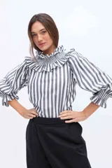 Blusa blanca de algodón con cuello alto fruncido con volados y mangas abullonadas con puños elásticos.