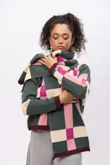 Saco de punto con diseño geométrico de cuadros en tonos verde, rosa, fucsia y crema. Presenta cuello redondo, cierre frontal con botones y terminaciones en color bordó.