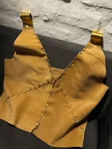 Top de cuero color marrón con costuras decorativas doradas y tirantes anchos.