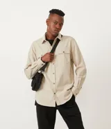 Camisa de corte regular, color beige, con cuello camisero, mangas largas, cierre frontal con botones y dos bolsillos con solapa en el pecho.