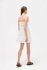 Vestido corto blanco de algodón con diseño de broderie, escote en V y tirantes finos. Presenta detalles de encaje y botones frontales.