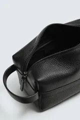 Neceser de piel negra con acabado abatanado, cierre de cremallera en el compartimento principal y un bolsillo interior también con cremallera. Incluye un asa de mano en un lateral.