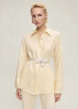 Camisa de lino color crema con cuello camisero, cierre frontal con botones metálicos y mangas largas con puños abotonados.