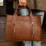 Cartera estructurada de cuero color marrón, con diseño de líneas definidas y dos bolsillos frontales con cierre vertical. Cuenta con doble asa de mano y correa desmontable.