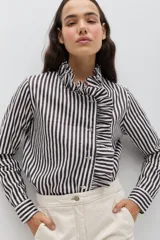 Camisa de algodón con estampado de rayas verticales en color negro y blanco. Presenta un diseño de cuello alto con volados y un detalle de volado asimétrico a lo largo de la botonadura frontal. Posee mangas largas con puños abotonados y un corte clásico.