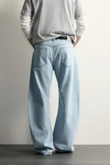Jeans de corte barrel fit confeccionados en denim de algodón rígido, con diseño de cinco bolsillos y cierre frontal con botones. Presentan un lavado claro con efecto de roturas en las perneras.