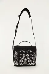Bolso tipo lonchera o cooler de la marca Farm Rio, color negro con estampado floral y tropical en blanco. Cuenta con cierre superior con cremallera, bolsillo frontal con cierre, asa de mano superior y correa ajustable para colgar al hombro o cruzado.