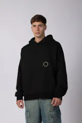 Buzo canguro oversize de frisa de algodón premium, color negro, con capucha y bolsillo frontal tipo canguro. Presenta un diseño con recortes horizontales y un logo circular bordado en el pecho.
