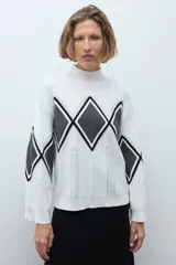 Media polera de tejido de punto color crudo, con diseño de rombos en el frente en tonos gris y negro. Presenta cuello alto y mangas largas.