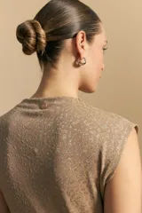 Top sin mangas de tejido texturizado con brillo integrado, color beige dorado, con cuello alto y hombros levemente estructurados.