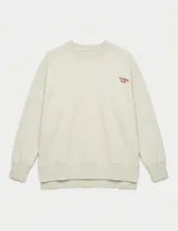 Buzo de cuello redondo en color beige, con diseño de corte holgado y mangas largas. Presenta un pequeño bordado en el pecho con la inscripción 'UNIFORM CLUB' en color naranja y un dobladillo asimétrico con tajo lateral.