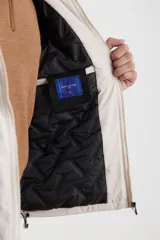 Campera impermeable negra con capucha, cierres a tono y cursores negros metalizados, bolsillos frontales con tapa, elásticos regulables en el ruedo e interior térmico con detalles confeccionados con láser.