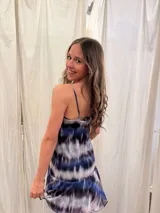 Vestido corto de tirantes finos con estampado tie-dye en tonos azul, negro y gris. Presenta un escote recto con frunce central y un volado en el ruedo de una textura diferente.