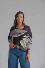 Sweater de punto con diseño abstracto en tonos negro, gris y blanco, con detalles en hilo dorado. Presenta cuello redondo, mangas tres cuartos con puños acanalados y un corte holgado.