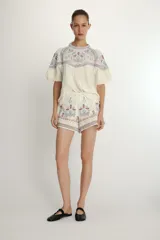 Shorts de tiro alto en color crudo con bordados decorativos en tonos azul y rojo. Presentan un diseño estructurado con cierre lateral oculto.