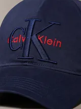 Gorra de béisbol azul marino con visera curva y parte trasera ajustable. Presenta el logo de Calvin Klein bordado en el frente con el monograma CK en azul oscuro y el nombre de la marca en rojo.