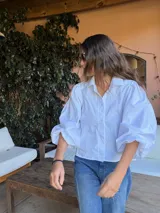 Camisa de color marrón oscuro con cuello clásico y mangas abullonadas con puños elásticos. Presenta un corte holgado y cierre frontal con botones.