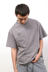 Remera de algodón con efecto lavado en color gris, de corte holgado y manga corta. Presenta un estampado cuadrado en la espalda con fondo marrón y círculos amarillos, junto con la inscripción CAPER.