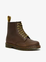 Bota Dr. Martens modelo 1460 de cuero marrón con aspecto desgastado y envejecido. Diseño de 8 ojales, con costuras amarillas, suela con amortiguación de aire resistente al aceite y lengüeta en el talón.