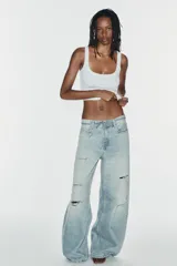 Jeans de tiro medio y corte baggy con cinco bolsillos, trabillas y rotos decorativos. Cuenta con detalle de cinturón confeccionado en el mismo tejido y cierre frontal con cremallera y botón metálico.