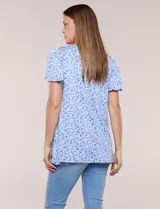 Blusa estampada en tonos de azul y blanco, con escote redondo, aplique artesanal bordado en el centro del pecho, mangas cortas tipo mariposa con volados y ruedo asimétrico.